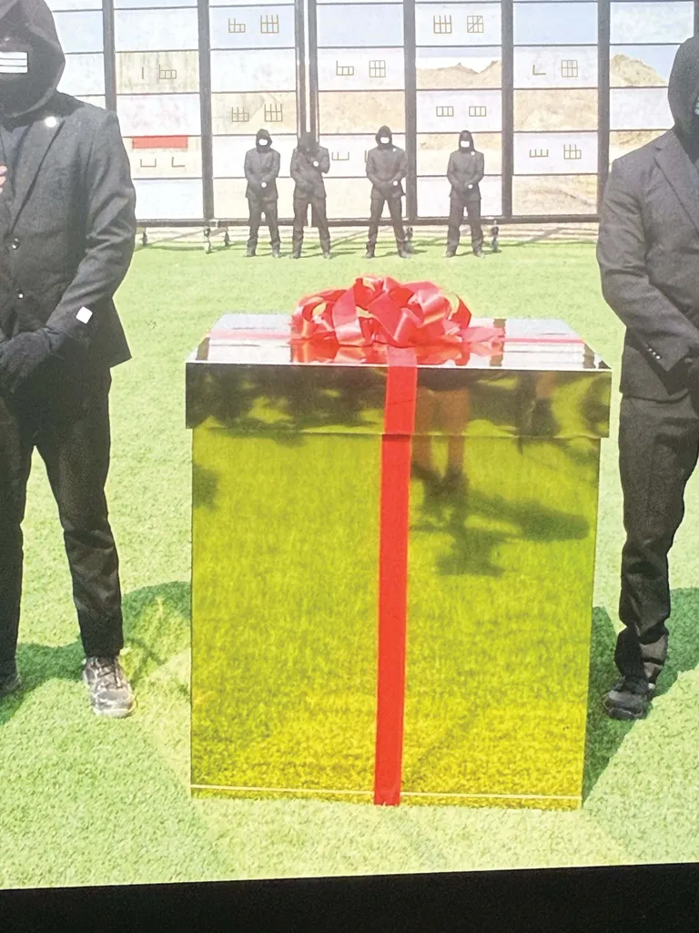 A large gold box with red ribbon with masked guards next to and behind it